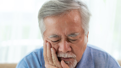 Older man holding his cheek in pain after dental trauma or a knocked-out tooth