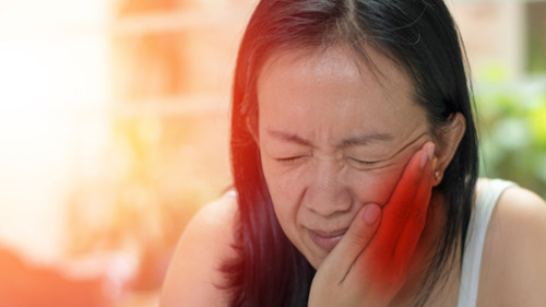 Woman grimacing in pain holding her jaw, illustrating acute oral trauma